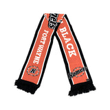 A Fort Wayne Black Komets knit scarf laid flat on a white background. The scarf features a bold orange and black color scheme with white lettering spelling 'BLACK' and 'FORT WAYNE', along with the team logo.